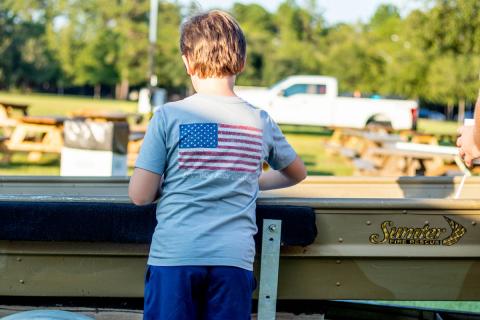 Boy in American Flag Shirt Standing at John Boat